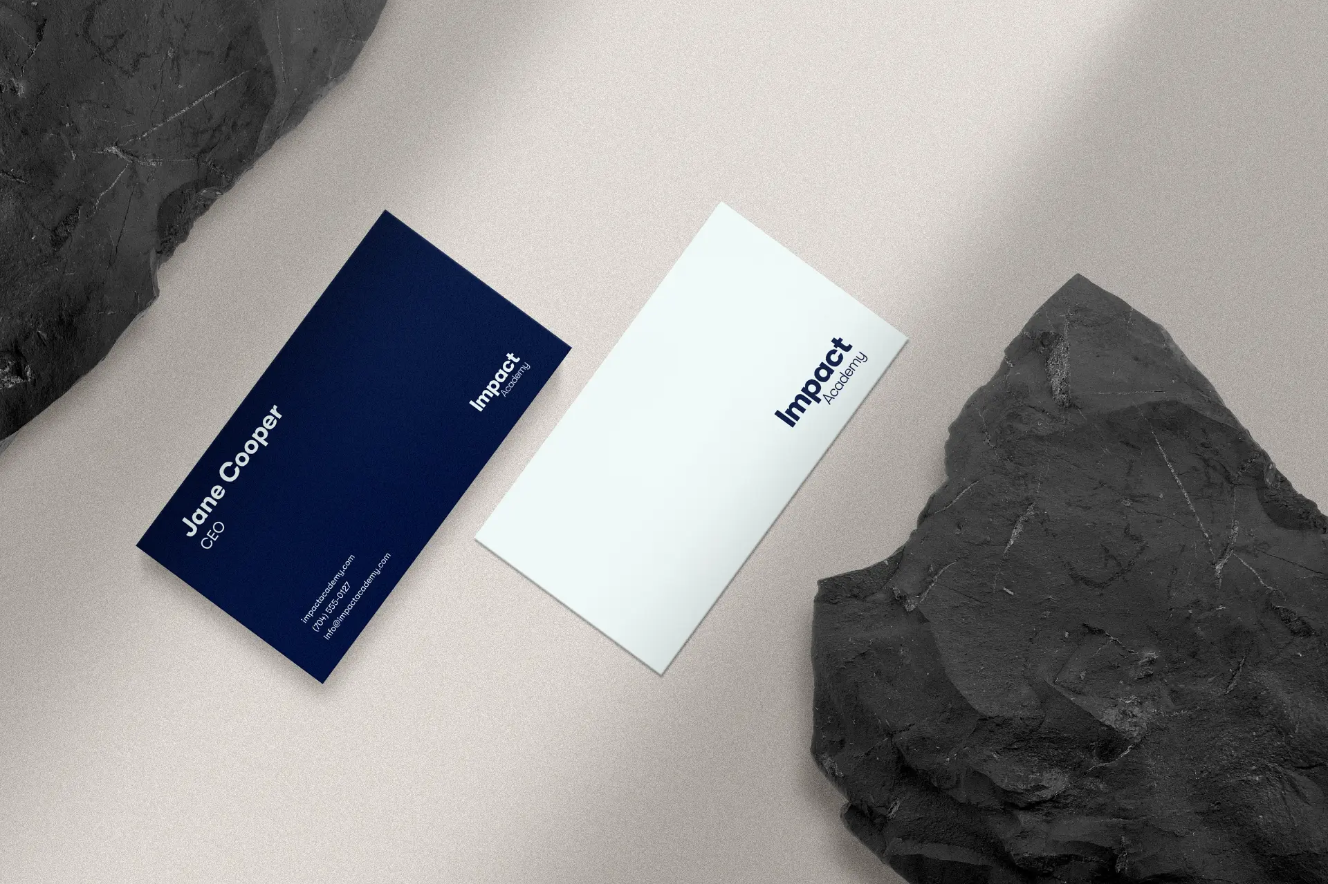 Impact Academy navy and white business cards styled beside dark stone.