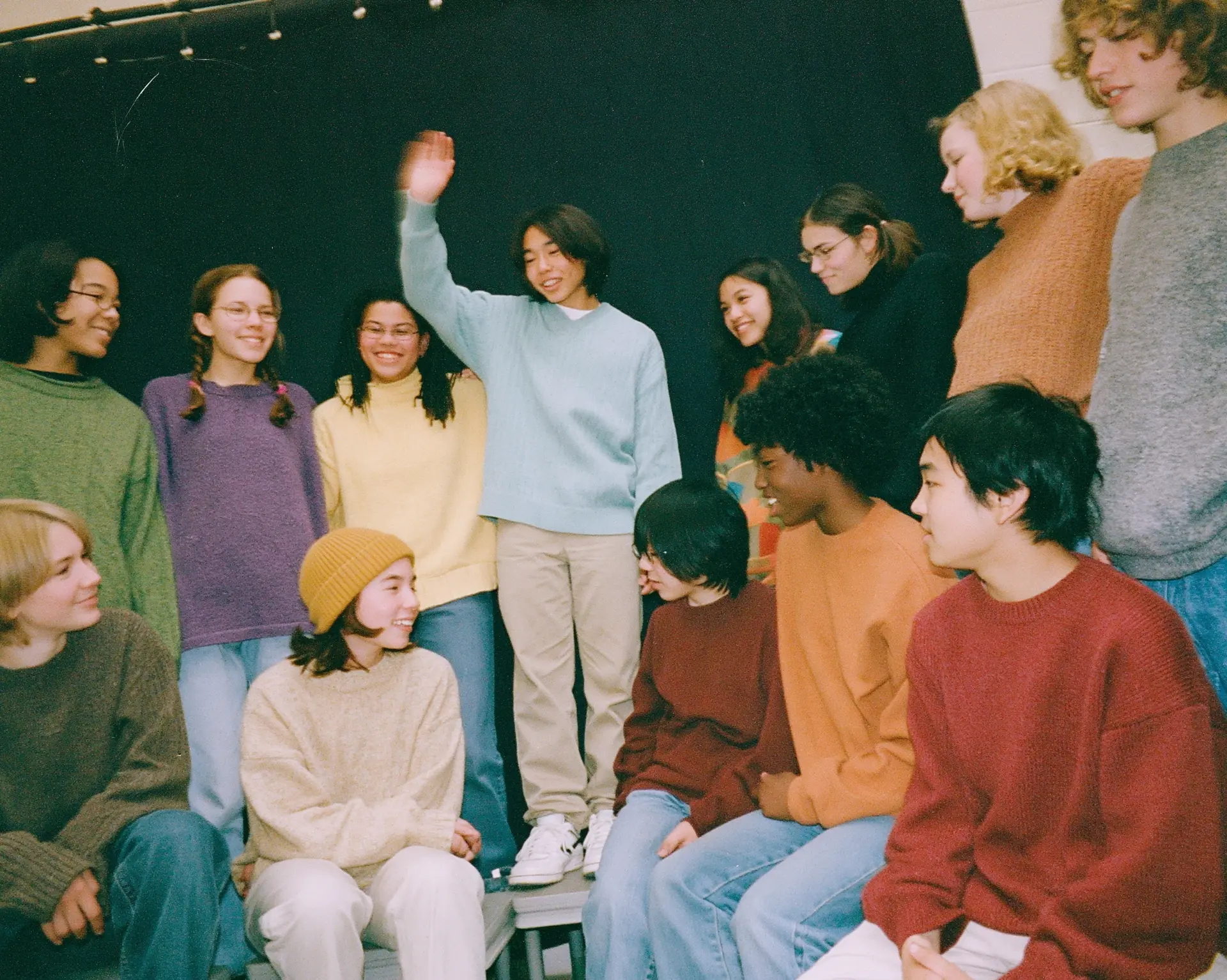 A diverse group of young people gathered together against a dark backdrop, in candid conversation.