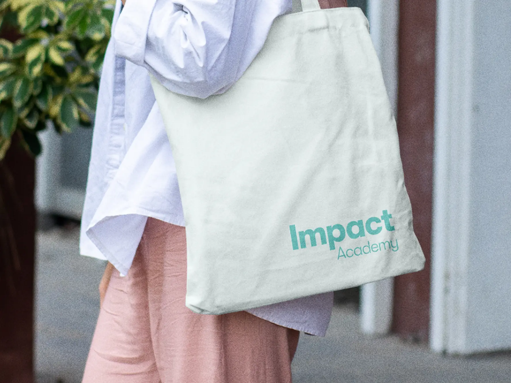 Person carrying a mint Impact Academy tote bag with the logotype in green.