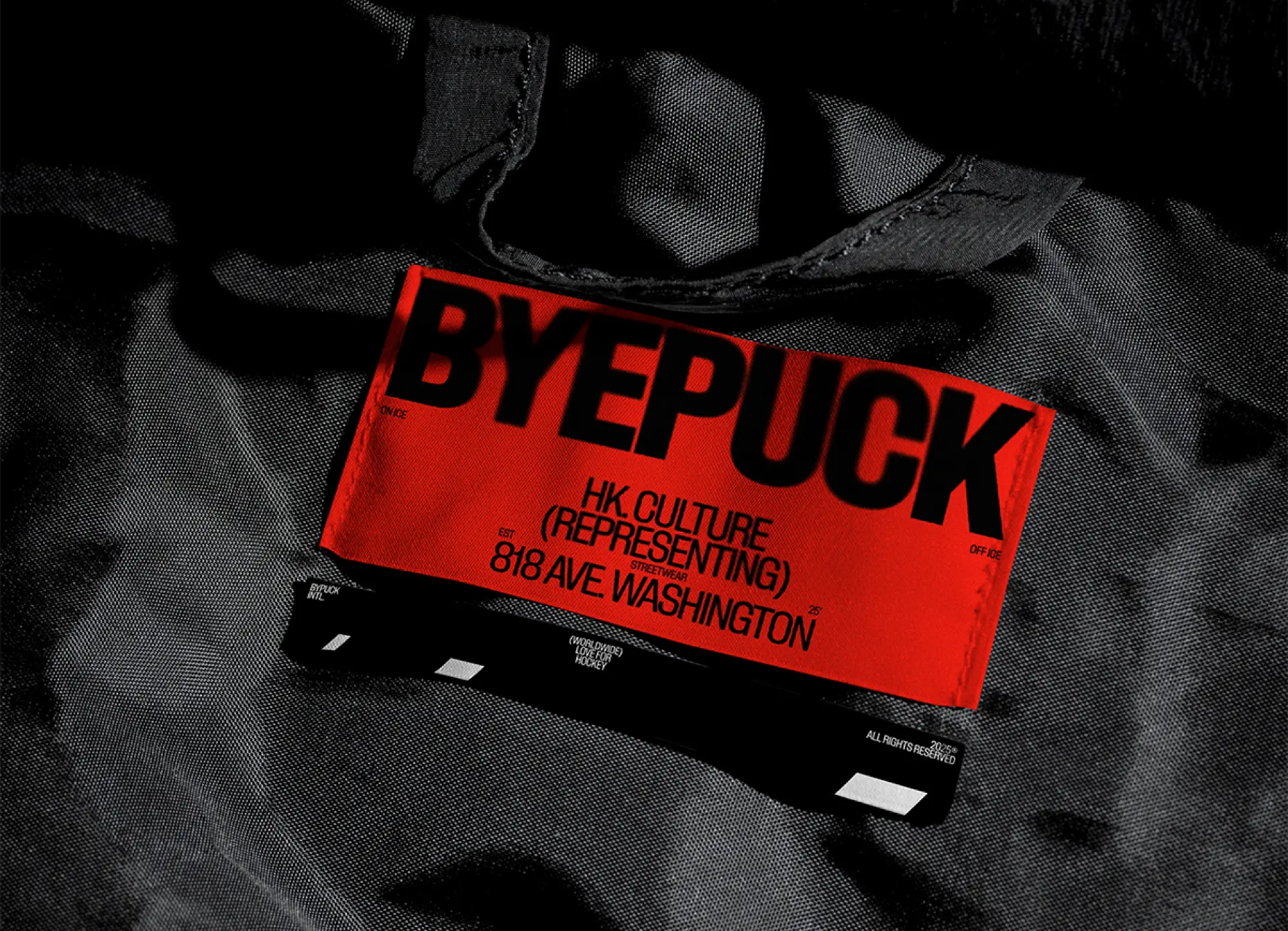 Bold red BYEPUCK packaging label lying on black athletic fabric, showcasing high-contrast streetwear-inspired print and packaging design.