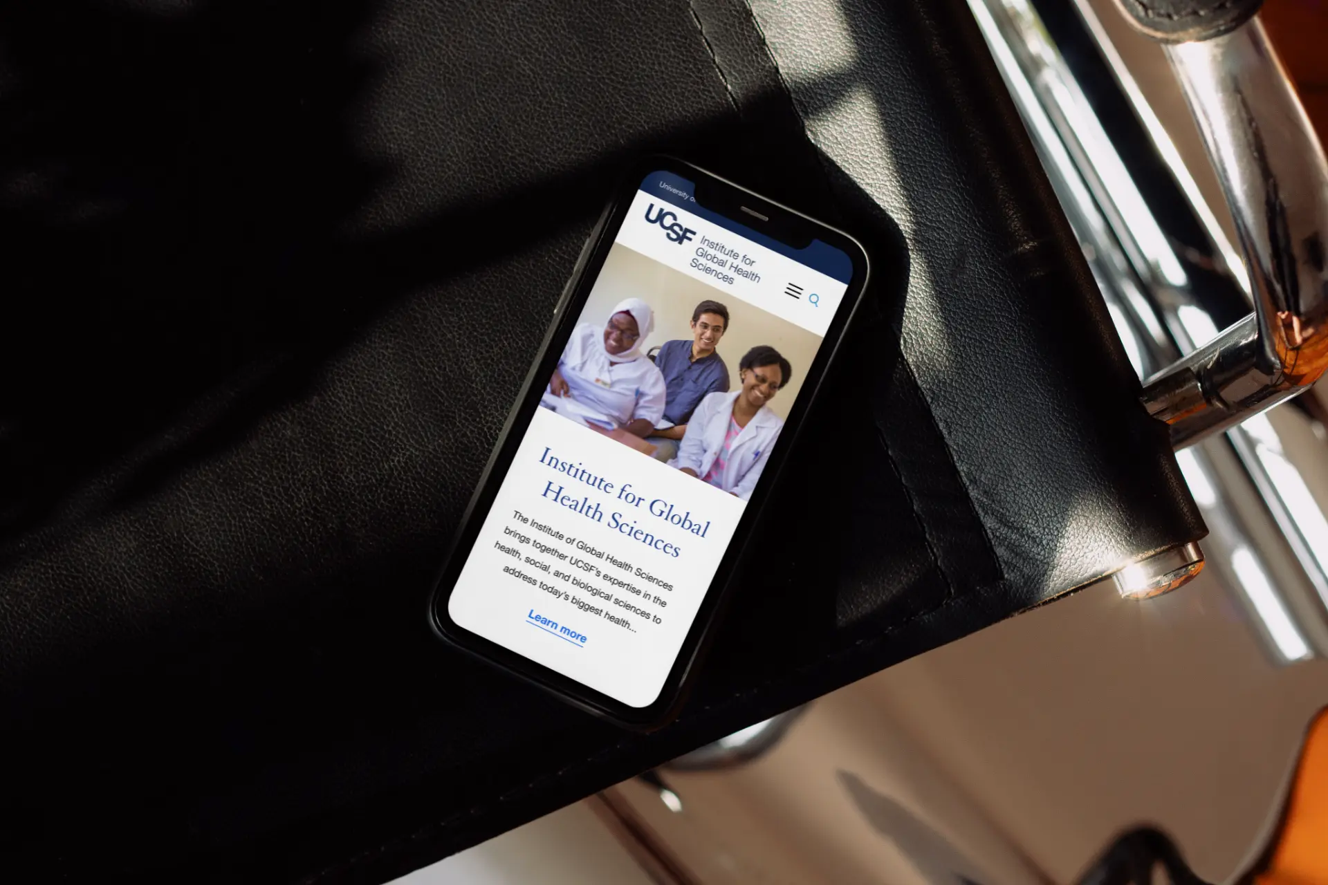 UCSF Institute for Global Health Sciences mobile homepage shown on a phone resting on a leather seat.